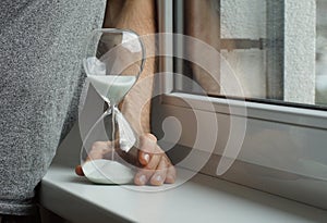 Man holding an hourglass and thoughtfully standing at a window boar