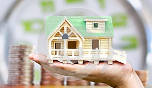 Man holding house model in his hand with coin and clock background. The concept of constructing a House, buying and selling