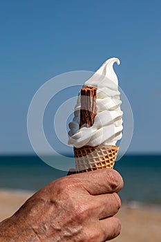 A man holding an ice cream cone at the beach, with a shallow depth of field