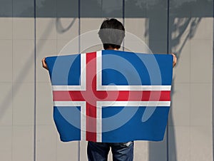 The man holding Iceland flag on his shoulder and turn back on grey background