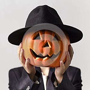 Man holding Jack o Lantern head in black hat over his face