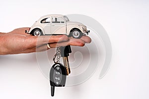 Man holding key and miniature automobile model on white background, closeup. Car buying