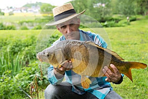 A man is holding a large carp fish caught on a fishing rod