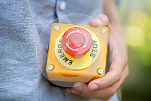 Man holding a large red industrial machinery emergency stop button in hand, object closeup detail, workplace occupational safety,