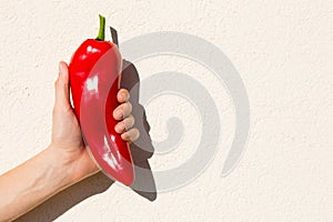 The man is holding a large red pepper in his hand.