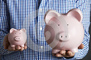 Man Holding Large And Small Piggy Bank