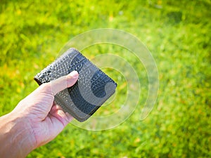 Man is holding leather wallet on green nature background