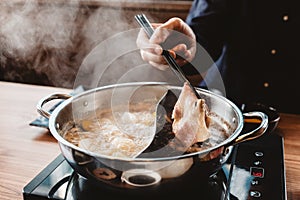 Man holding medium rare slice Wagyu A5 beef out from hot pot shabu shoyu soup base by chopsticks with steam