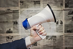 A man holding a megaphone on background of newspapers. News message concept