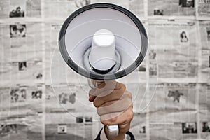 A man holding a megaphone on background of newspapers. News message concept