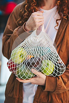 A man is holding a mesh material bag of fruit in his hand.