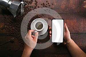 Man holding mobile phone and coffee cup on wooden background with coffee beans.