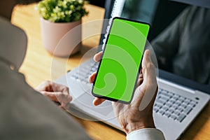 man holding mobile phone in hand with blank green screen. mockup