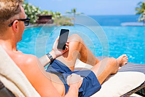 Man holding mobile phone while relaxing by the pool.