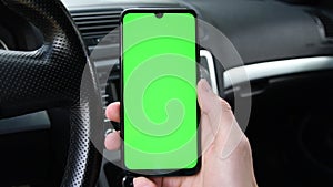 Man holding mobile phone, smartphoneon the background of a black car interior. Green screen, blank phone, application.Swipe to the