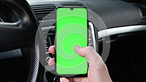 Man holding mobile phone, smartphoneon the background of a black car interior. Green screen, blank phone, application.Swipe to the