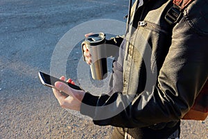 Man holding mobile phone and thermo cup, travel mug.