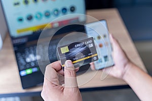 Man holding mock up credit card with number using smartphone and laptop computer for shopping.