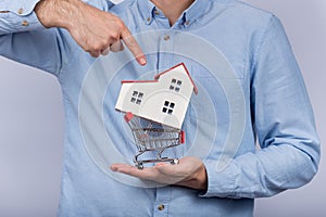 Man holding model home in shopping cart. Buying house concept