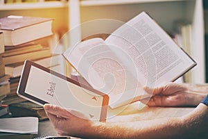 Man holding a modern ebook reader and book in library