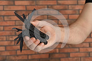 Man holding multitool near brick wall, closeup