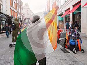Man holding National flag of Ireland in focus. Grafton street of Dublin city out of focus in the background. Support or protest