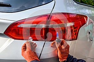 Man holding new lamps near car headlamps