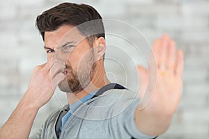 man holding nose and showing stop gesture with palm