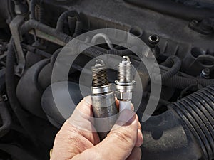 Man Holding old and new car spark plugs on engine background