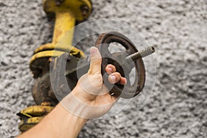 Man holding old weathered gas crane on the background of a gray wall. Old gas gate of yellow colour is on a pipe and