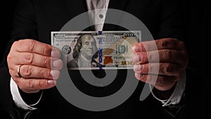 man holding one hundred dollar bills in his hands on a black background