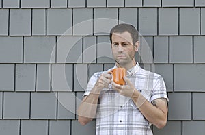 Man holding an orange coffee cup with two hands with a gray background.