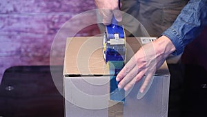 Man holding packing machine and sealing cardboard box with duct tape