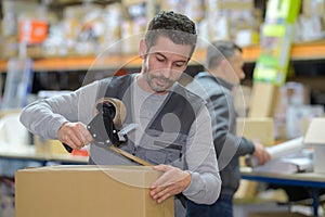 Man holding packing machine and sealing cardboard boxes