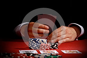 Man holding a pair of playing cards while playing poker with chips and cards in front of him