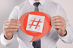 Man holding paper speech bubble with hashtag symbol on light background, closeup