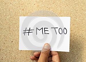 Man holding paper with text  METOO handwritten on a white card with a cork board background