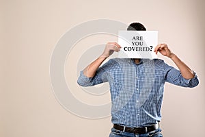 Man holding paper with text ARE YOU COVERED? on background, space for text. Insurance concept