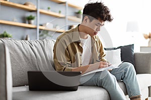 Man holding paper, writing and working on laptop at home