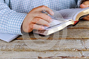 Man is holding a pen in his hand with an open Holy Bible lying in fornt of him