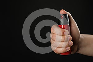 Man holding pepper spray on black background, closeup. Space for text