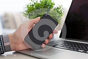 Man holding phone in hand on laptop notebook keyboard