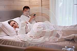 Man holding phone in hands and looking at sleeping lady