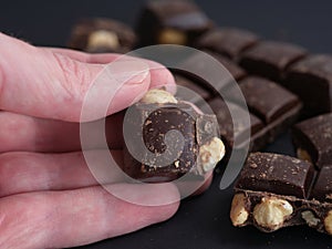 A man holding a piece of dark chocolate with hazelnuts in his hand