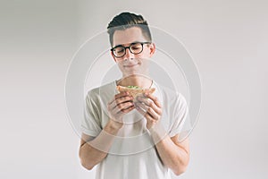 Man holding a piece of hamburger. student eats fast food. not helpful food. very hungry man. Nerd is wearing glasses.