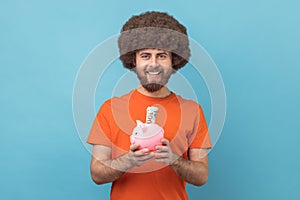 Man holding piggy bank with dollar banknote in hands, being happy of savings.