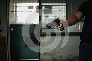 Man holding a pistol, standing in a room in black, pointing and aiming a gun at a target. concept of assassination, murder,