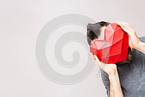 Man holding polygonal diamond shaped red heart in front of his face