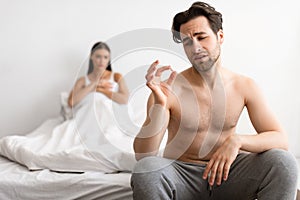 Man Holding Potency Pill While Girlfriend Waiting For Sex Indoor