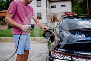 Man holding power supply cable at electric vehicle charging station.